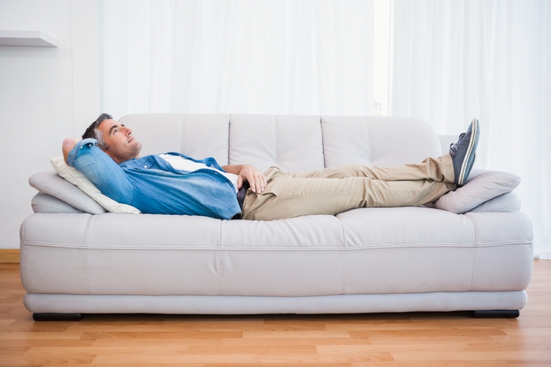 Smiling man lying and relaxing on the couch at home in the living room